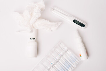 Flat lay with some sealed vials or ampoules, nasal and oral spray, thermometer and paper napkins.