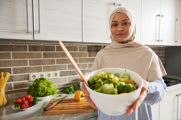 Arab Muslim woman holds a bowl with salad and shows it to the camera - Powered by Adobe