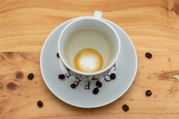 empty coffee cup on a wooden table with scattered roasted coffee beans