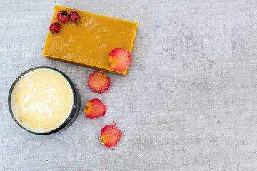 Handmade soap bar with rose petals, rosehips, and cocoa butter as a base for soap on wooden table. Spa photo on rustic background. Aromatherapy and natural hygiene products concept. Space for text.