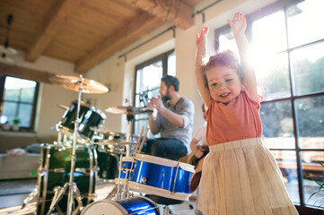Portrait of small children with father indoors at home, playing drums.