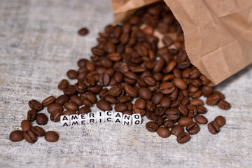 close up of Freshly roasted coffee beans near word AMERICANO written with little white cubes. top view