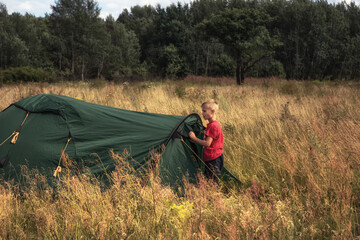 Happy child boy standing by camping tent on camping site during summer holidays in countryside concept for happy childhood lifestyle © splendens