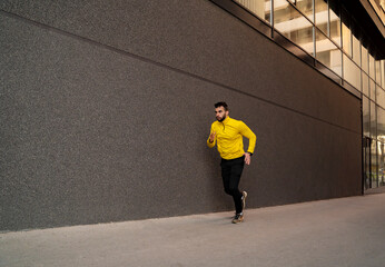 Man running next to black modern wall in the city, image contains motion blur 