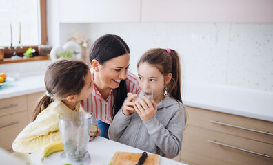 Mother with girls indoors at home, preparing fruit smoothie drink.