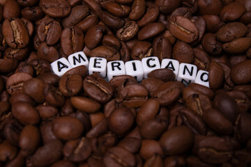 close up of Freshly roasted coffee beans near word AMERICANO written with little white cubes. top view