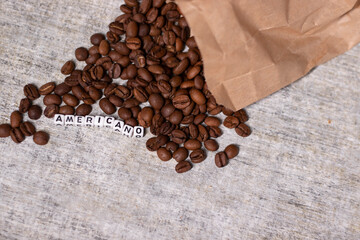 close up of Freshly roasted coffee beans near word AMERICANO written with little white cubes. top view