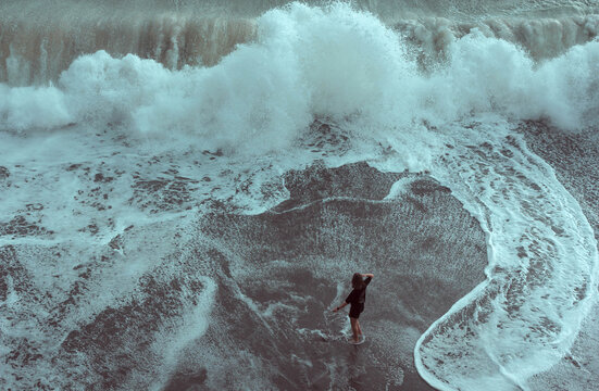 A Woman Stands Alone In Front Of A Large Tidal Wave Going To The Beach