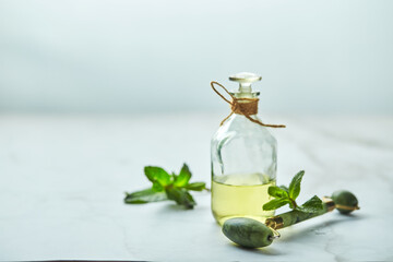 Bottle of essential oil of mint and green leaves and jade massage roller for the face. Natural organic ingredients for cosmetics, skin care, body care. Beauty care concept