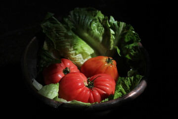 still life, consisting of pink tomato lettuce leaves and lying in an antique dish, surrounded by a dark background