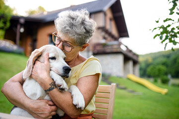 Close-up portrait of senior woman sitting outdoors in garden, pet dog friendship.