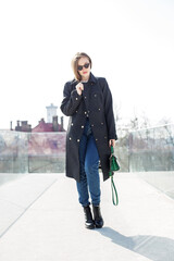 Young girl wearing sunglasses with long blonde hair in the wind, wearing a long coat outside