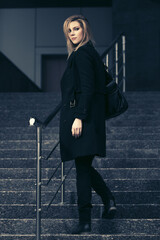 Fashion blonde business woman in black coat with leather handbag on steps