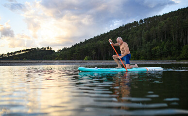Fototapeta na wymiar Senior man paddleboarding on lake in summer. Copy space.