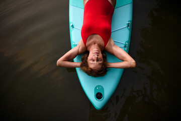 Top view of senior woman lying on paddleboard on lake in summer, resting.