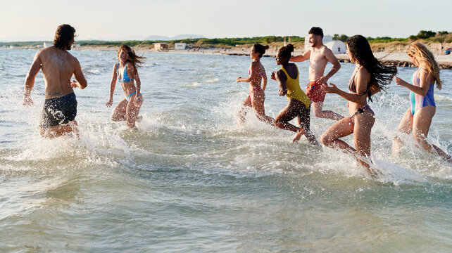 Laughing friends running into the ocean