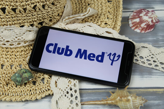 Viersen, Germany - March 1. 2021: Closeup of smartphone with logo lettering of club med travel agency with sun hat and shells on wood table