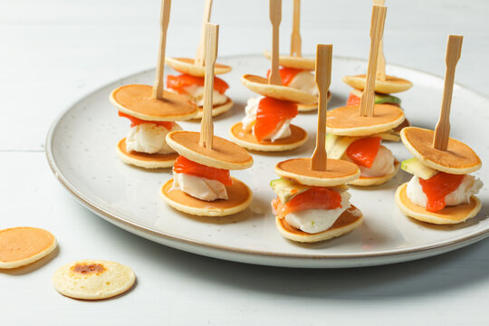 A dish with mini pancake sandwiches, cream cheese and salmon. Close-up, horizontal with space