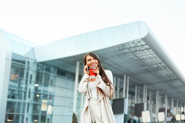 Beautiful Business women talking by smartphone at street. Girl have conversation speaking by mobile with cup of coffee in hand.