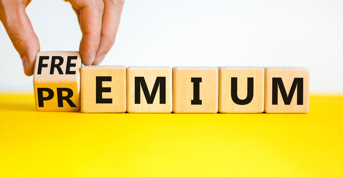 Premium or freemium symbol. Businessman turns the wooden cube, changes the word 'premium' to 'freemium'. Beautiful yellow table, white background. Business, premium or freemium concept. Copy space.