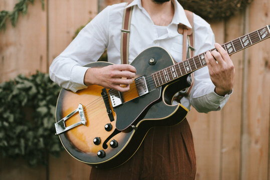 close up of young man wearing brown pants and suspenders playing the guitar