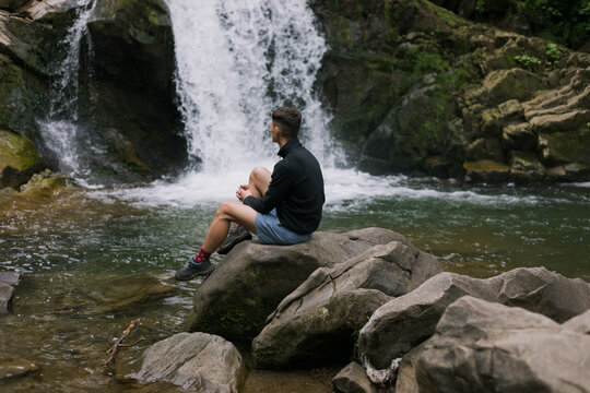 the guy sits on the stones against the background of the waterfall