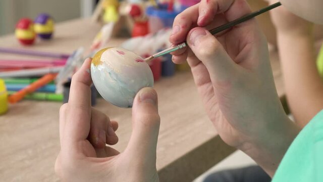 Close-up of a girl's hands painting an Easter egg with paint and a brush. Drawing of a smiling smiley face. 4k video.