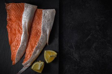 sliced fresh raw salmon lying sideways on a stone cutting board with lemon wedges on a black textured concrete background. top view. sea food concept with copy space