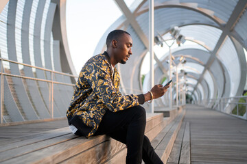 Cool Black Man Sitting With Phone Outdoors.