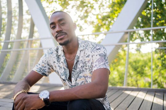 Young Black Guy Sitting And Looking At Camera Outdoors.