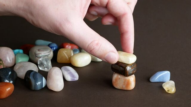 Person is forming a pyramid of smooth stones. Pile of colorful gemstones