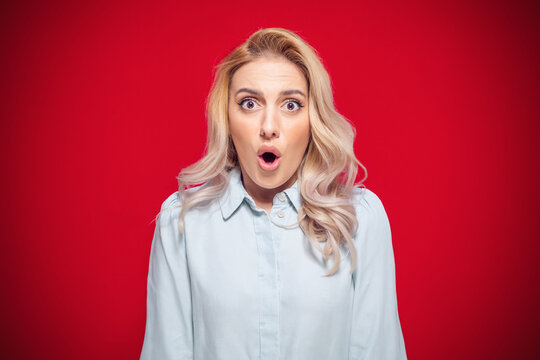 Surprised face of woman stare to camera, isolated on red background. Surprise expression face - head of a amazed girl. Wao - omg concept