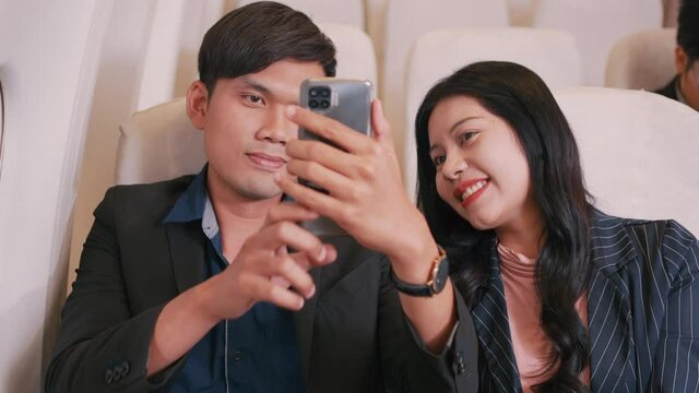 Asian Businessman and Businesswoman taking photo selfie with smartphone together enjoying moment, Couple business team on the plane flight, Business class, Airplane concept. 4K UHD Footage.