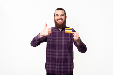 Happy young man with beard in shirt showing credit card and thumb up