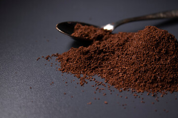 gold teaspoon in a pile of ground or instant coffee on dark background