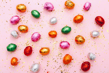 Easter chocolate mini eggs wrapped in a colorful foil, scattered on a pink background with golden confetti