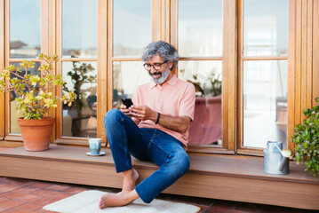 Relaxed mature man texting in a sunny terrace