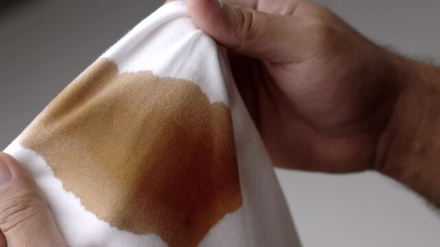 White cotton shirt A lot of stains, stains, coffee stains, man's hand holds the shirt up and spreads it to look dirty Must be brought to the washing machine