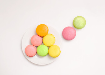Fototapeta na wymiar Almond cookies Flat lay photo in minimal style Orange, pink, green, and yellow macarons on small plate on white table