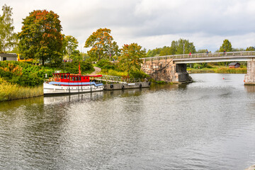 A boat docks along the banks of the Porvoonjoki river as visitors cross the bridge connecting to the medieval village of Porvoo, Finland.
