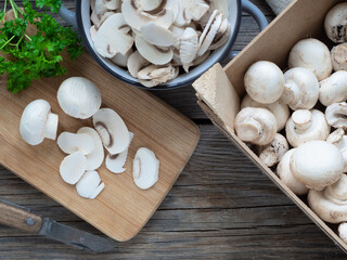 Raw mushrooms, whole and sliced, lined from a wooden board box and placed in a metal pot. Light onions and parsley leaves.