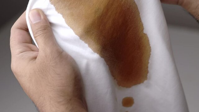 White cotton shirt A lot of stains, stains, coffee stains, man's hand holds the shirt up and spreads it to look dirty Must be brought to the washing machine