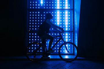 Woman on bicycle at night against blue neon background