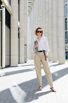 Smart woman with laptop standing on street near business center