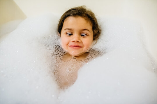 Young girl making silly face laying in a bubble bath.