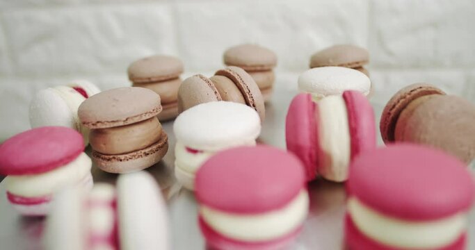 Close up of colorful white, red, and caramel chocolate macarons dessert, filling with tasty ganache, on the table at light kitchen or confectionery shop. Panorama multi-colored French almond macaroons