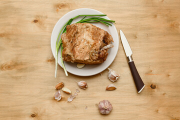 baked meat on a plate, green onion and garlic on wooden background, home cooking