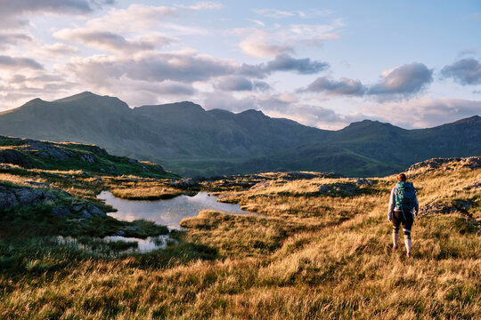 Female walker on Hard Knott looking towards Sca Fell at sunset. Lake District, Cumbria, UK.