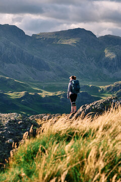 Female walker on Hard Knott looking towards Sca Fell at sunset. Lake District, Cumbria, UK.