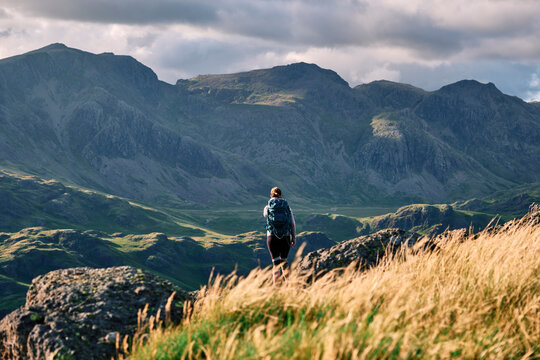 Female walker on Hard Knott looking towards Sca Fell at sunset. Lake District, Cumbria, UK.